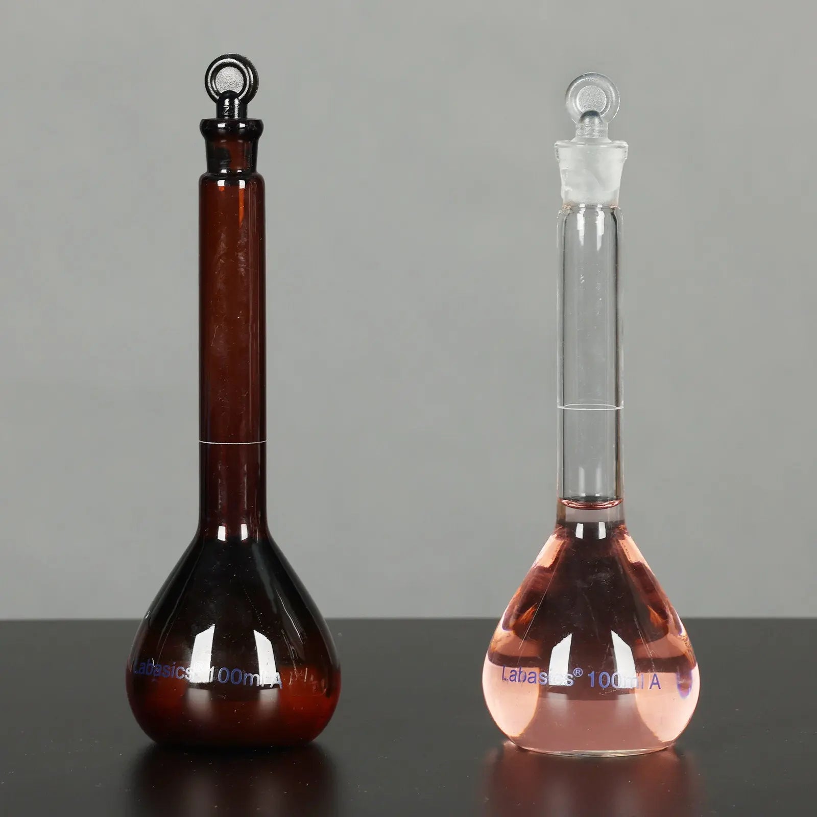 Amber volumetric flask and clear glass volumetric flask 100 ml side by side for comparison